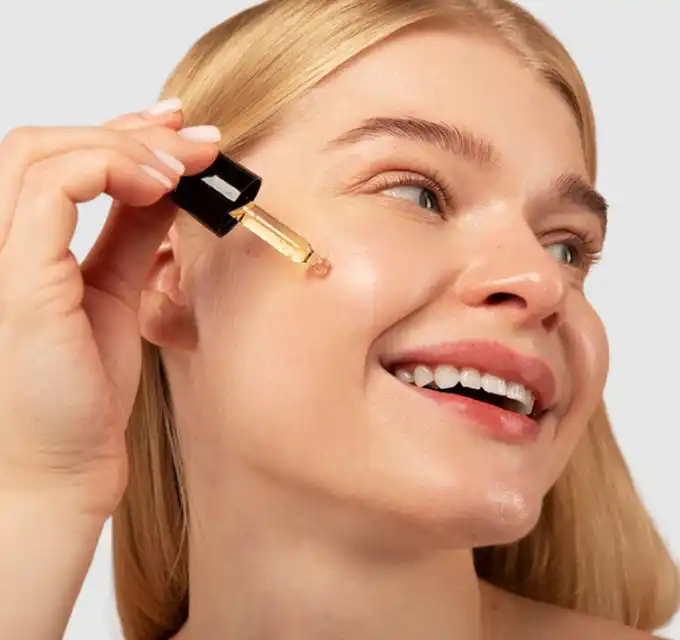 Close-up of a woman applying serum with a dropper on a neutral background — clean product/application shot