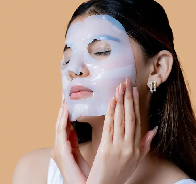 "Skincare portrait of a model gently cupping the chin with hands on a warm beige background, highlighting hydrated skin and jewelry."
