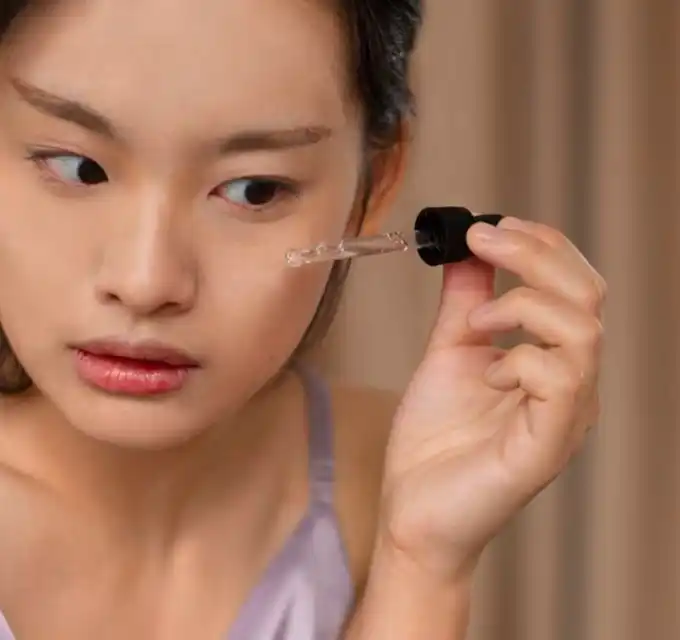 Tight close-up of a woman carefully applying a serum with a dropper to her cheek — demonstrates product application for scar-fading routines