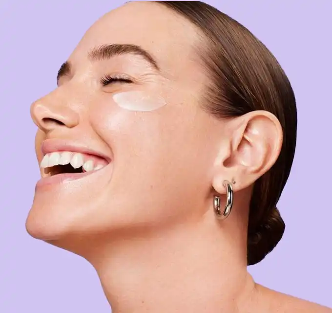 a woman's lower face and ear showing an under‑eye patch on a pale lilac background