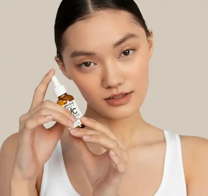 Model posing with a vitamin C serum bottle in a hero shot with editorial text about fine lines and wrinkles, neutral background